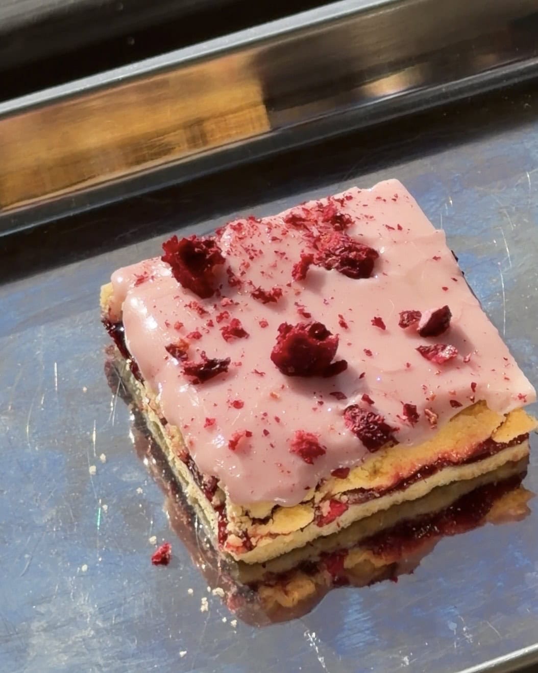 Overhead view of a cherry raspberry jam bar with cherry glaze and freeze dried cherries on a stainless steel baking tray.