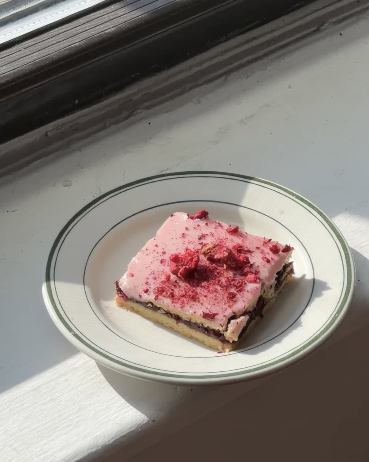 Side view of a Cherry Raspberry Jam bar with cherry glaze and freeze dried cherries on a white and green plate.