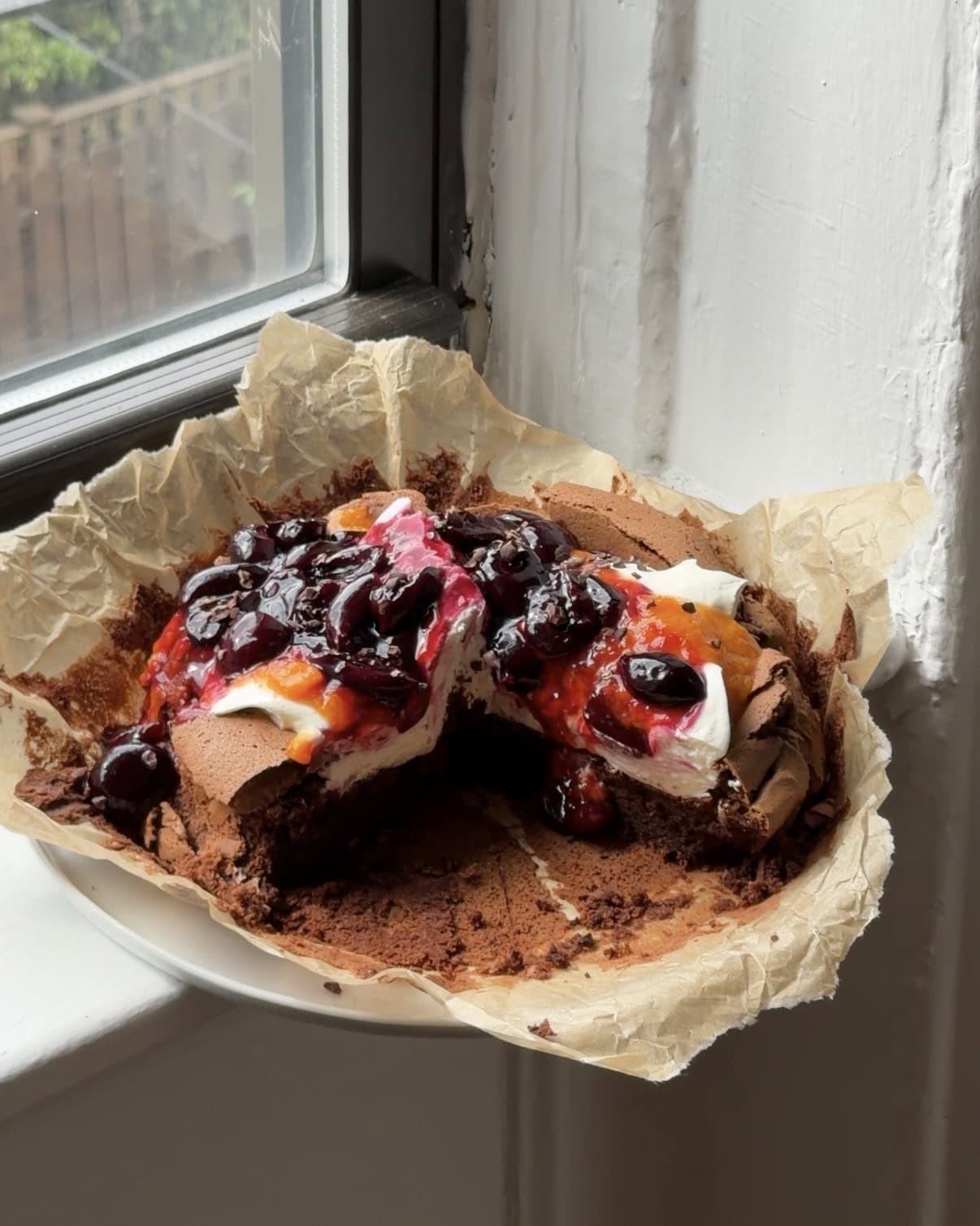 Side view of a Flourless Chocolate Cherry Cake topped with whipped cream, apricot compote, and saucy cherries.