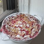 Side view of a red currant clafoutis dusted with powdered sugar in a white staub pie pan.