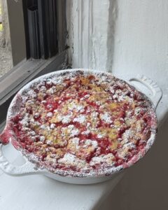 Side view of a red currant clafoutis dusted with powdered sugar in a white staub pie pan.