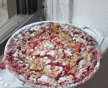 Side view of a red currant clafoutis dusted with powdered sugar in a white staub pie pan.