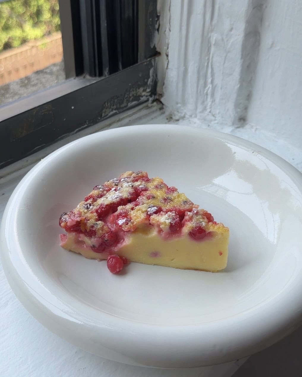 Side view of a slice of red currant clafoutis on a white plate.