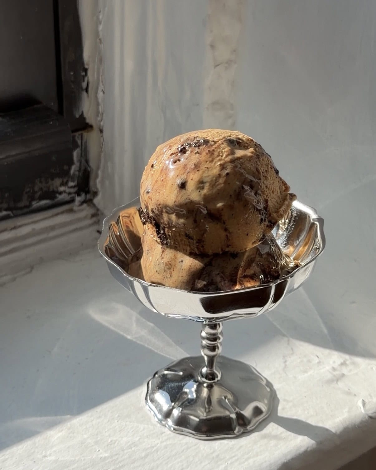 Side view of two scoops of Coffee Oreo Fudge Ice cream in a vintage silver coupe cup.