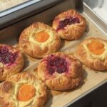 Side view of apricot and raspberry cream cheese danishes on a parchment lined baking sheet.