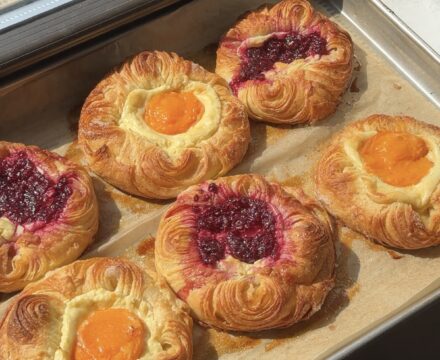 Side view of apricot and raspberry cream cheese danishes on a parchment lined baking sheet.