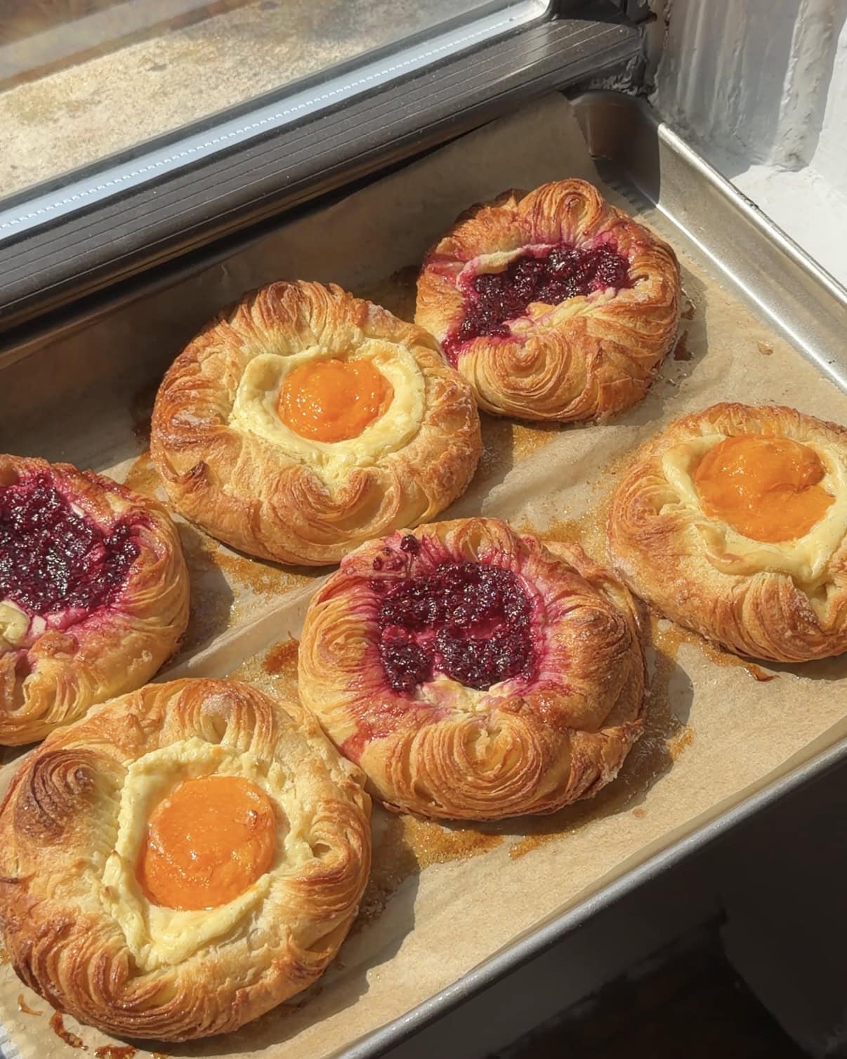 Side view of apricot and raspberry cream cheese danishes on a parchment lined baking sheet.