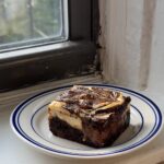 Side view of a slice of caramelized banana cream cheese brownie on a white and blue plate.