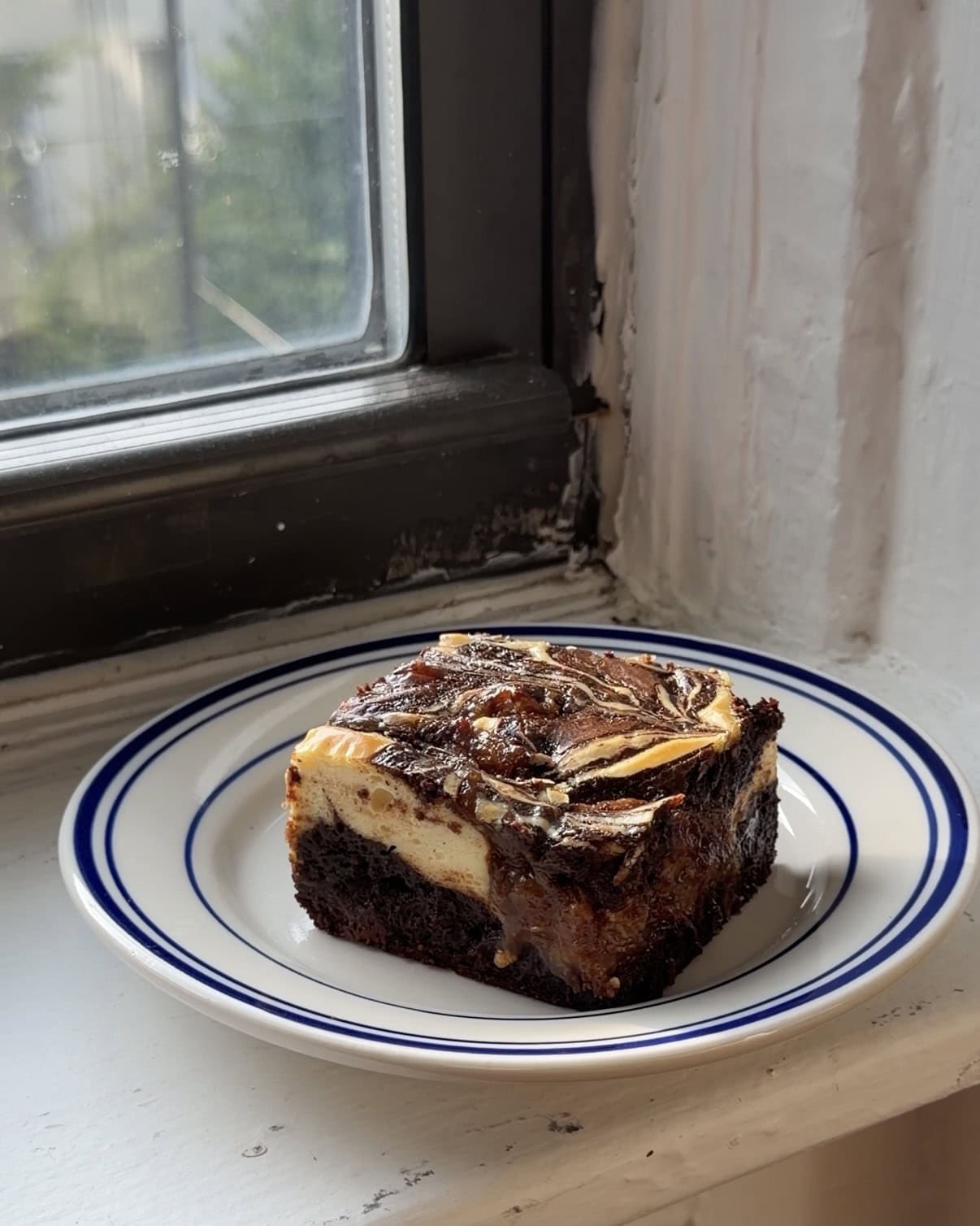 Side view of a slice of caramelized banana cream cheese brownie on a white and blue plate.