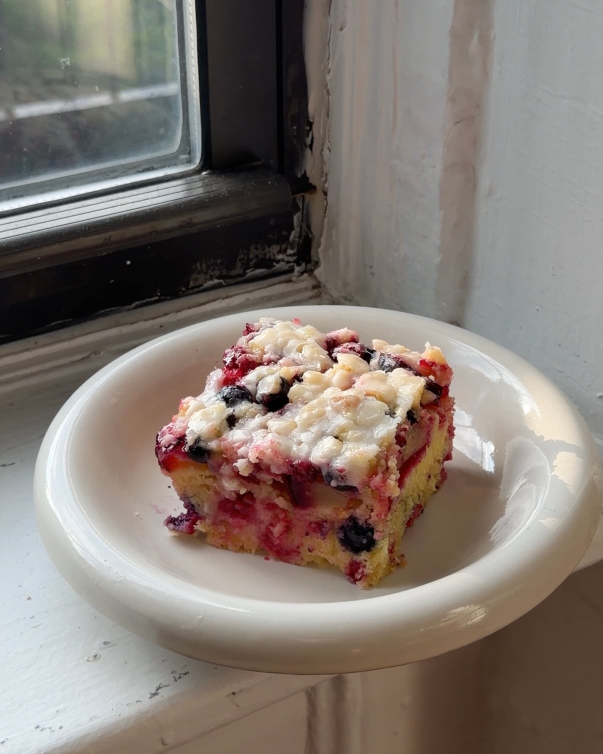 Side view of a slice of Plum Berry Crumb Cake topped with lemon glaze on a white plate.