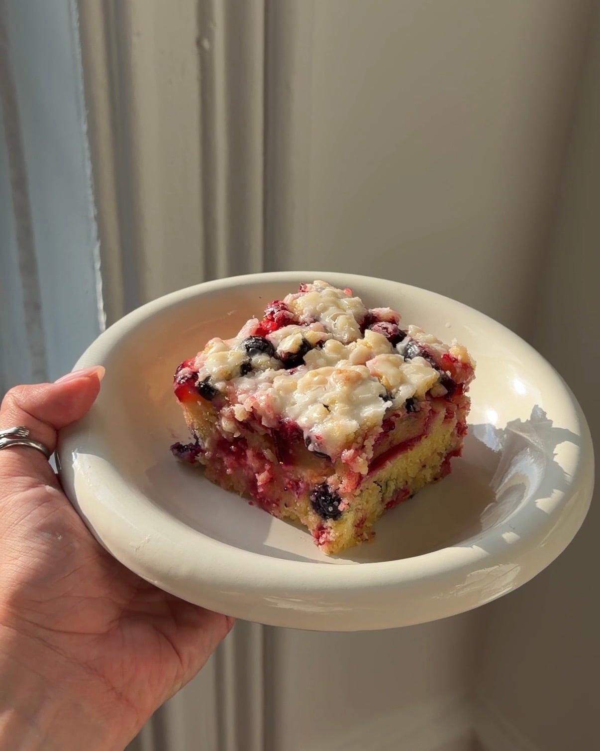 Side view of a slice of Plum Berry Crumb cake on a shallow white bowl in the sun.
