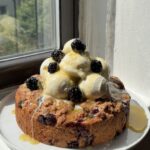 Side view of a Blackberry Blueberry Biscuit cake topped with vanilla bean ice cream and honey butter sauce.