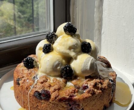 Side view of a Blackberry Blueberry Biscuit cake topped with vanilla bean ice cream and honey butter sauce.