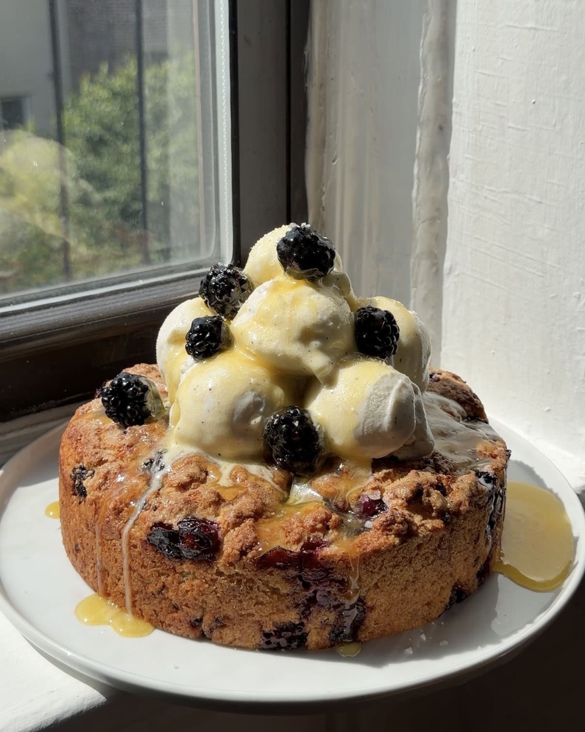 Side view of a Blackberry Blueberry Biscuit cake topped with vanilla bean ice cream and honey butter sauce.
