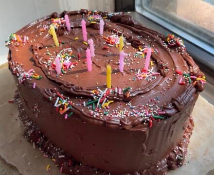 Side view of a Brown Butter Cake with Chocolate Cream Cheese Frosting decorated with rainbow sprinkles and candles.