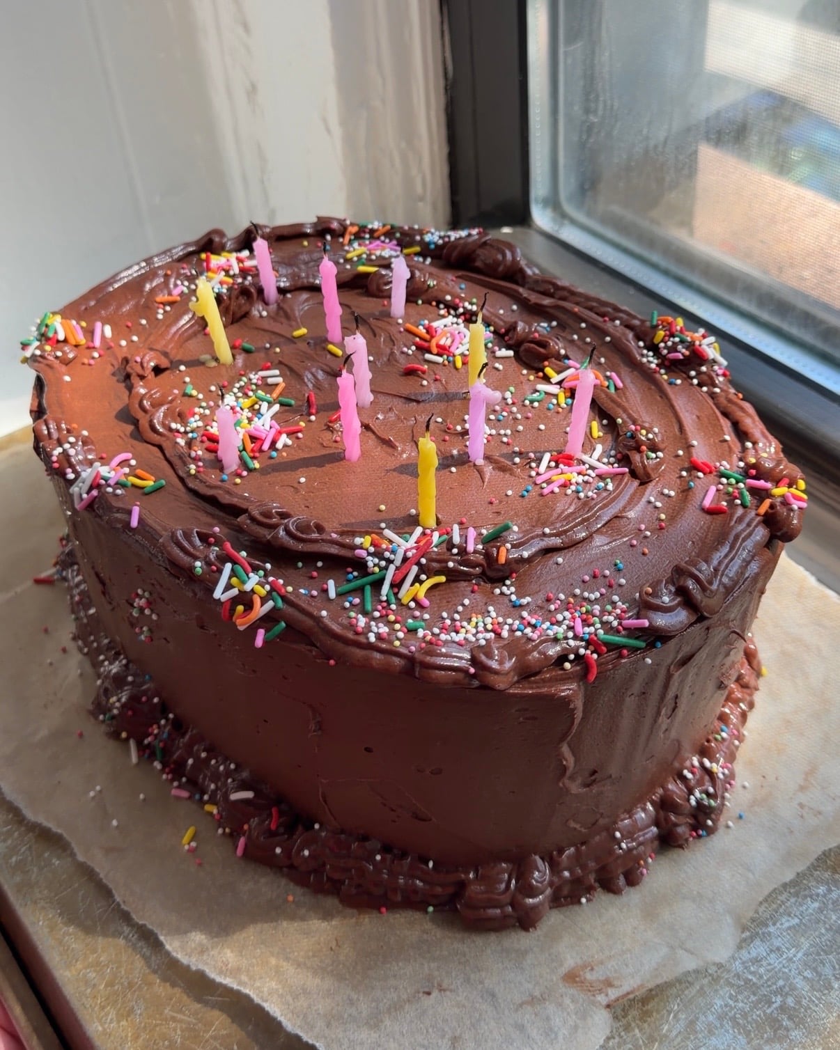 Side view of a Brown Butter Cake with Chocolate Cream Cheese Frosting decorated with rainbow sprinkles and candles.