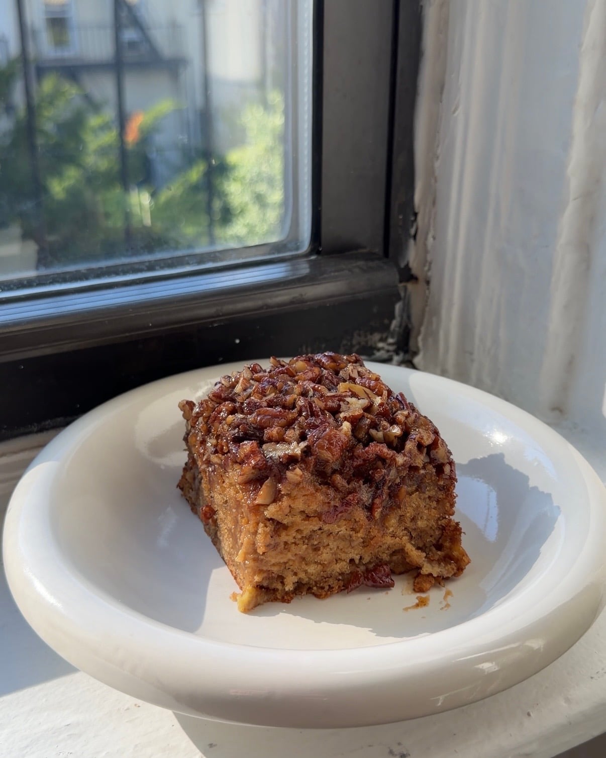 Side view of a square slice of Banana Bread Pecan Upside Down Cake on a white plate.