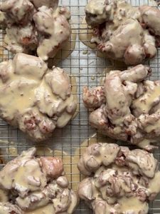 Overhead view of 6 apple fritters with a maple glaze on a wire cooling rack.
