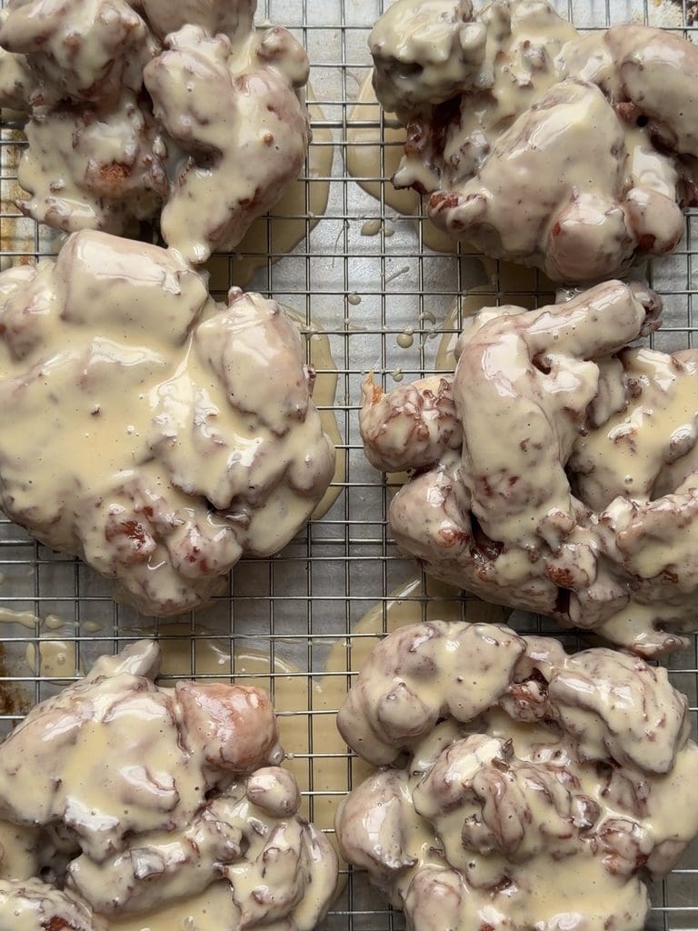 Overhead view of 6 apple fritters with a maple glaze on a wire cooling rack.