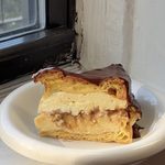 Side view of a slice of Boston Cream Pie Karpatka on a white bubble plate.