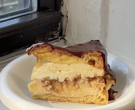 Side view of a slice of Boston Cream Pie Karpatka on a white bubble plate.