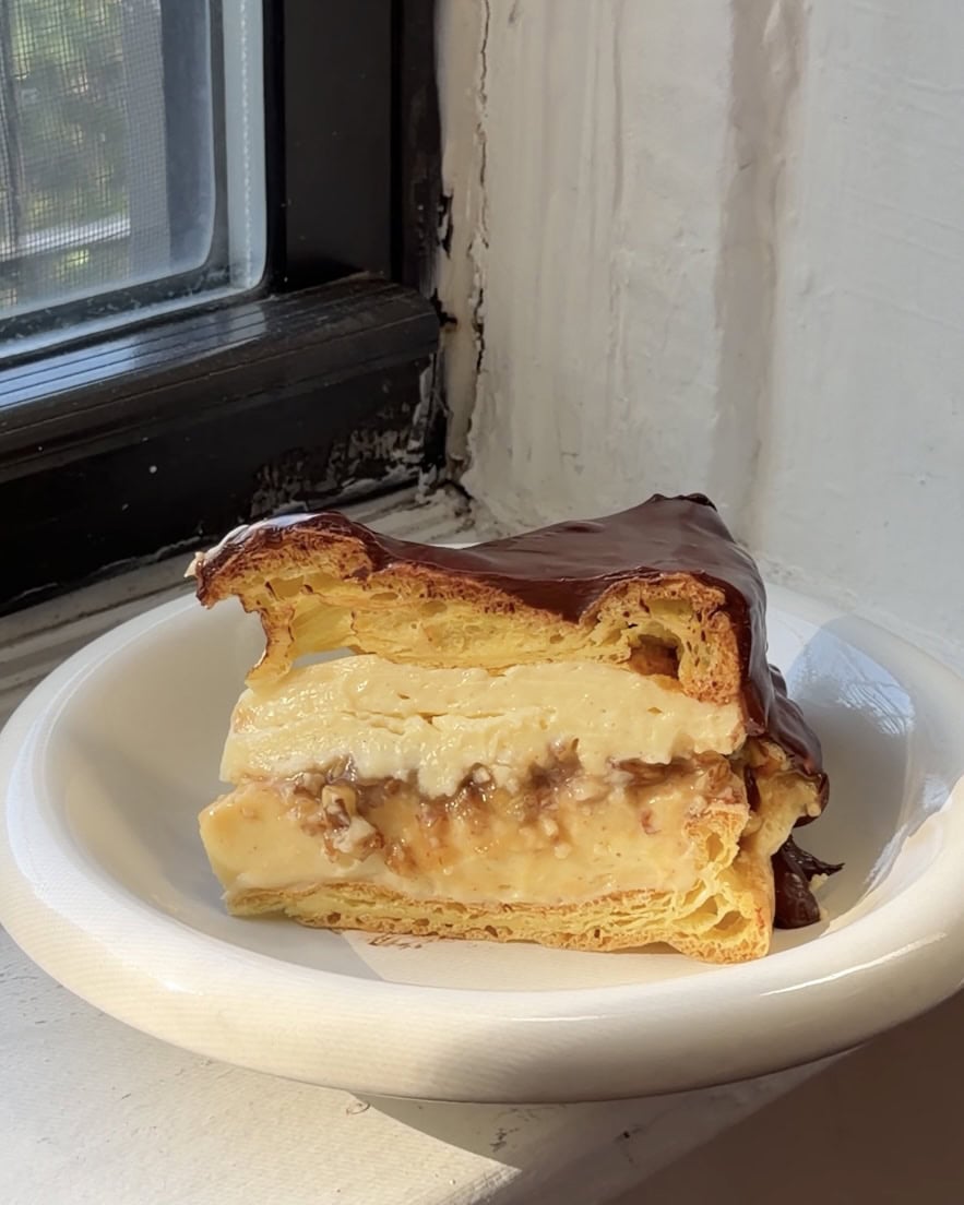 Side view of a slice of Boston Cream Pie Karpatka on a white bubble plate.