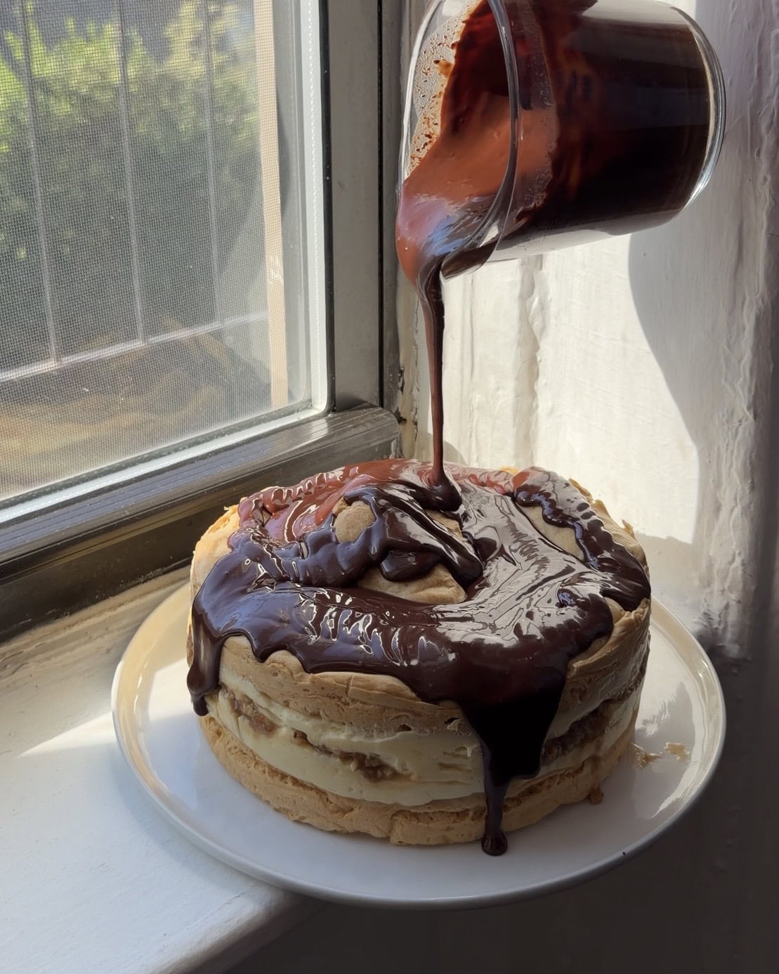 Full Boston Cream Pie Karpatka on a large white plate with chocolate ganache being poured over top.