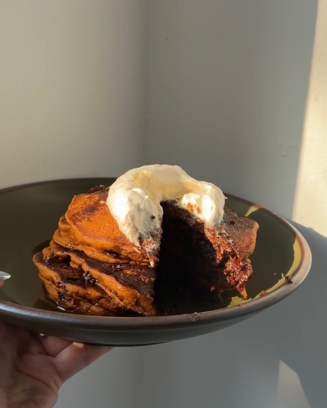 A stack of brown butter chocolate chip pancakes topped with maple syrup and whipped cream and a bite taken out.