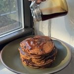 Side view of a stack of brown butter chocolate chip pumpkin pancakes being topped with maple syrup.